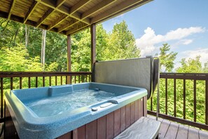 Een hottub op een houten terras, met uitzicht op een bos.