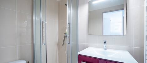 A bathroom with a glass-enclosed shower, a white toilet, a red vanity with a white sink, and a mirror above the sink.