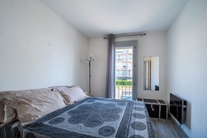 Un dormitorio con cama, mesita de noche, espejo y vistas a un balcón exterior.