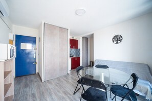 Un espacio habitable compacto con kitchenette, una zona de comedor con mesa y sillas, y un sofá.