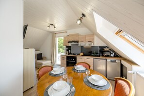 En matplats med ett runt bord för fyra personer, ett kök med moderna vitvaror och ett loftliknande tak med takfönster.