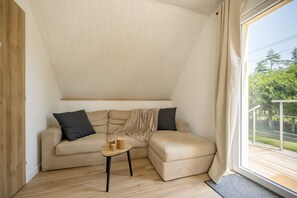 Ein Eckzimmer mit einer Couch, einem kleinen Tisch und Blick auf Grünfläche.
