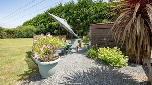 A patio area with a table and chairs, a large umbrella, and a wooden shed. - Au pas de côté plourhannais - Proche Plage (Plourhan)