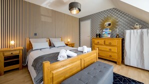 A modern bedroom with a sloped ceiling, a wooden bed, a bench, a dresser, and a vanity with a mirror. - Au pas de côté plourhannais - Proche Plage (Plourhan)