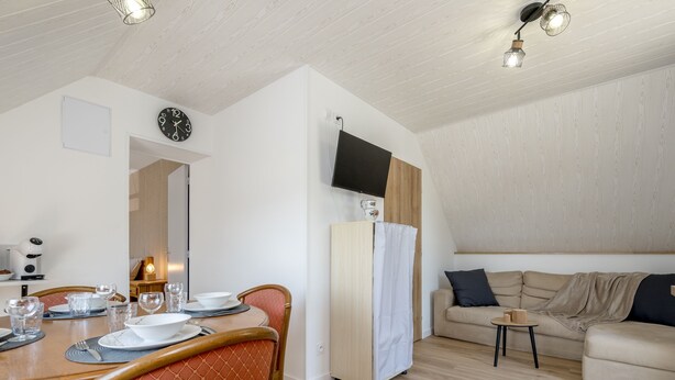 A modern living room with a dining area, a flat-screen TV mounted on the wall, and a wooden ceiling. - Au pas de côté plourhannais - Proche Plage (Plourhan)