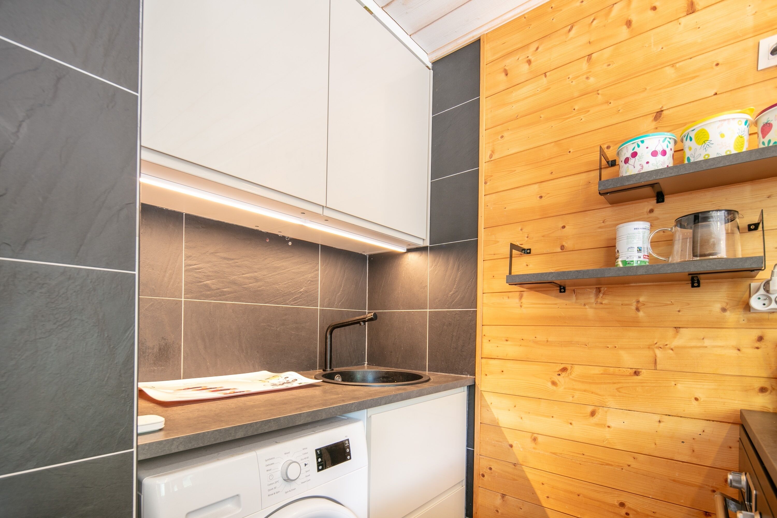 Eine kleine Küche mit Waschmaschine, Spüle und Holzböden mit Behältern.