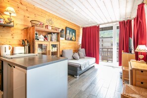 Ein gemütliches Zimmer mit Holzvertäfelung, einer Couch, einem Esstisch und Blick durch ein großes Fenster.