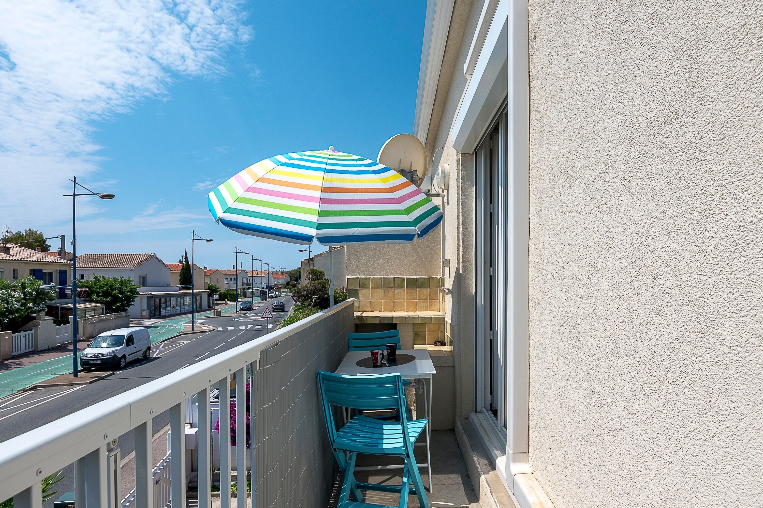 Un balcon avec un parasol à rayures, une table et deux chaises.
