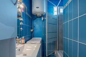 Ein Badezimmer mit einem weißen Waschbecken, einem Spiegel, einer Dusche und einer blauen Fliesenwand.