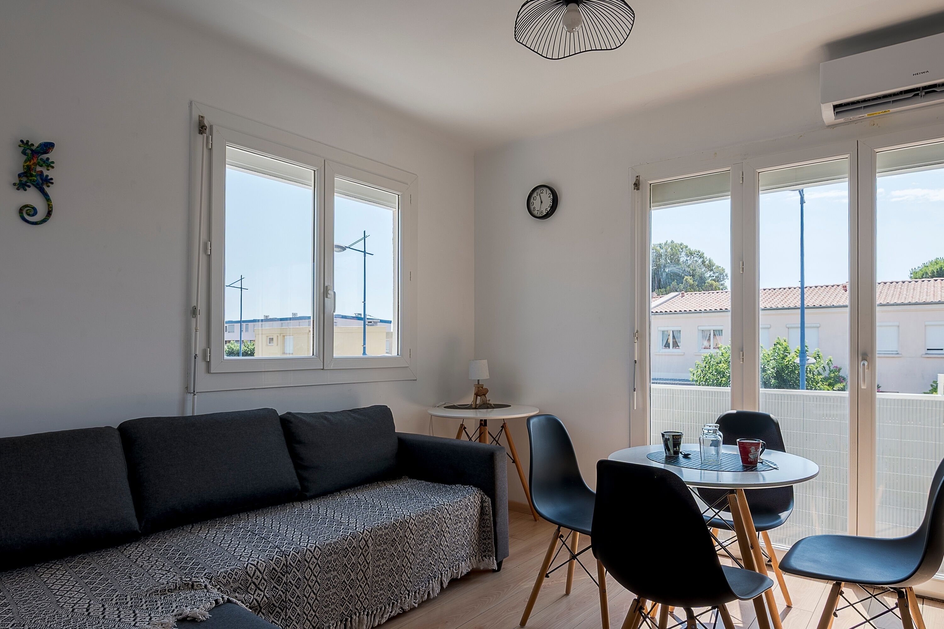 Et værelse med en sofa, et spisebord med stole, et lille bord med en lampe og et vindue med udsigt til bygninger.