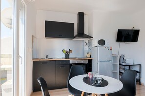 Eine moderne Küche mit Einbauofen, schwarzem Herd und Mikrowelle. Ein Esstisch mit zwei Stühlen und ein kleiner Couchtisch ergänzen das Bild.