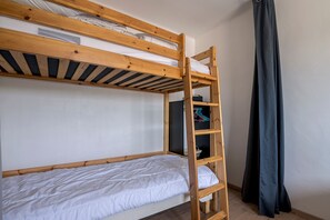 Un letto a castello con scala in legno, un letto singolo in basso e una piccola unità scaffale con una pentola e una borsa.