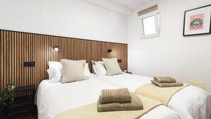 Ein Hotelzimmer mit einem Bett, Nachttischen, einer Wandlampe, einem kleinen Fenster und einem gerahmten Bild an der Wand.