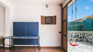 Ein Zimmer mit Tischtennisplatte, Dartscheibe und Blick auf Schwimmbad und Außenbereich.