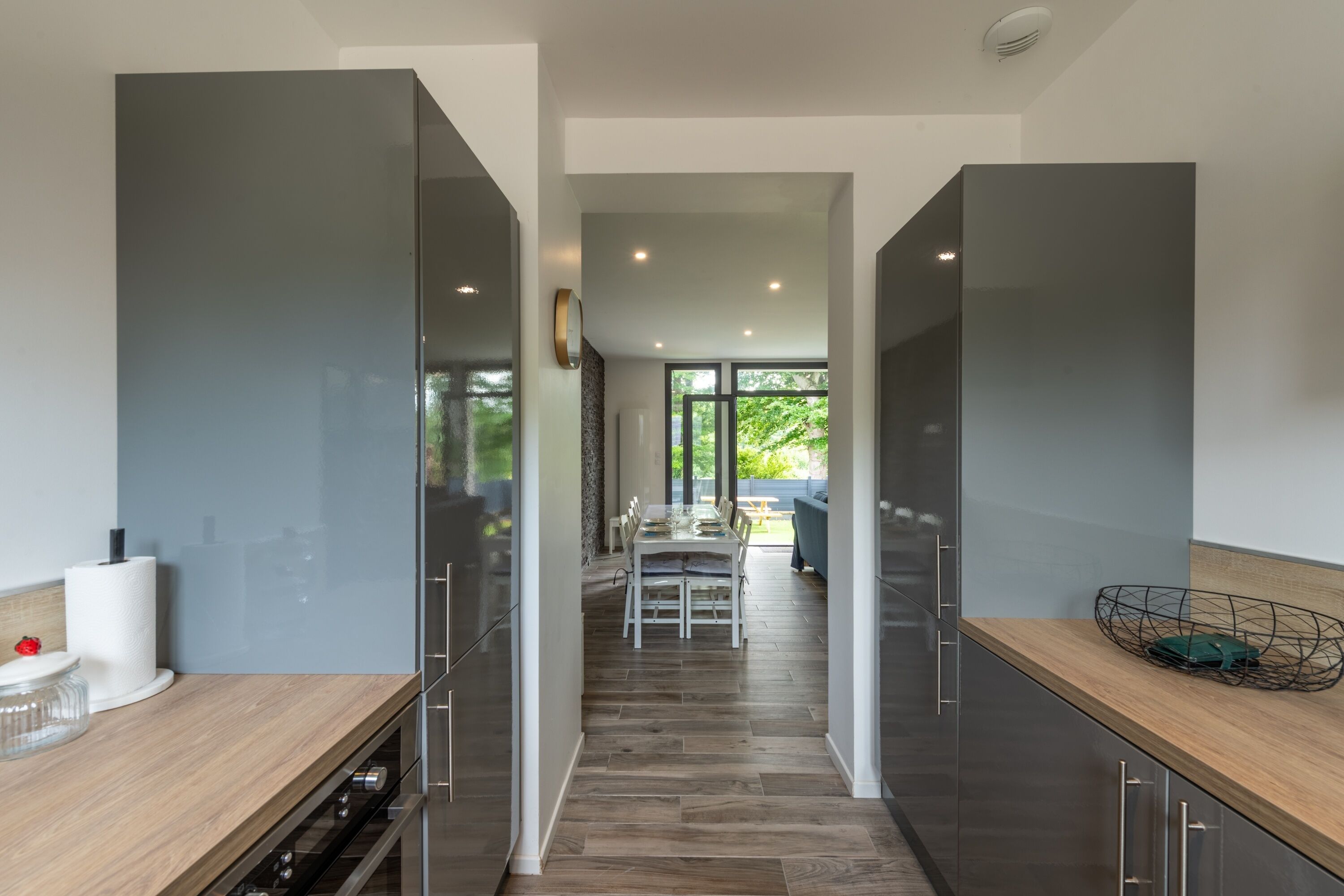 A modern kitchen with dark cabinetry, a wooden countertop, and a dining area with a table and chairs.