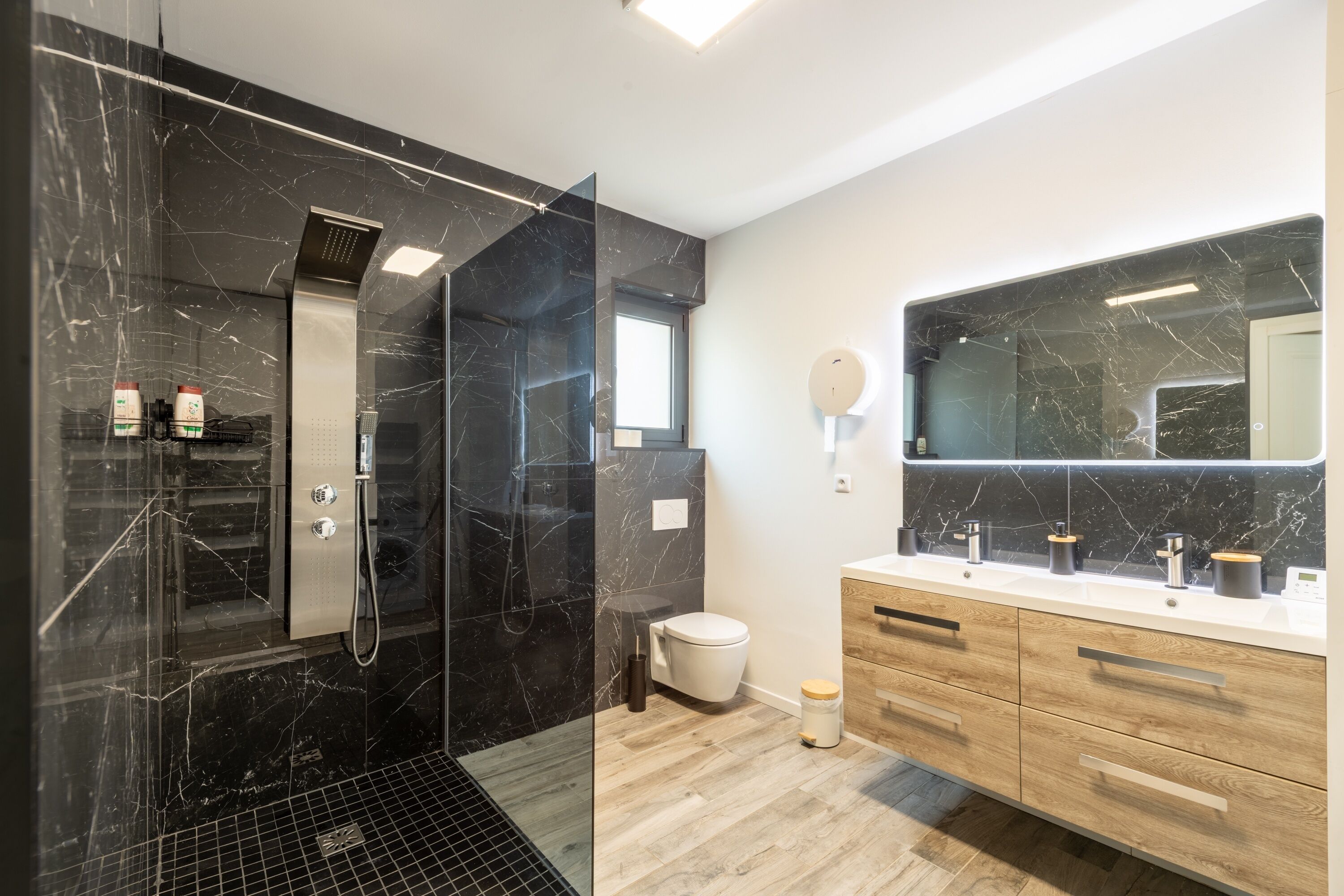 Une salle de bain moderne avec une douche à parois de verre, un grand miroir et des meubles en bois.
