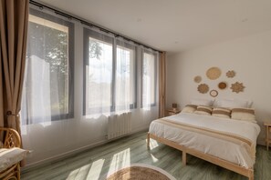 A bedroom with a large window, a bed with white bedding, a wooden floor, and a wall with decorative wall art. - Le Beau Rivage - 1km de la Plage (Criel-sur-Mer)