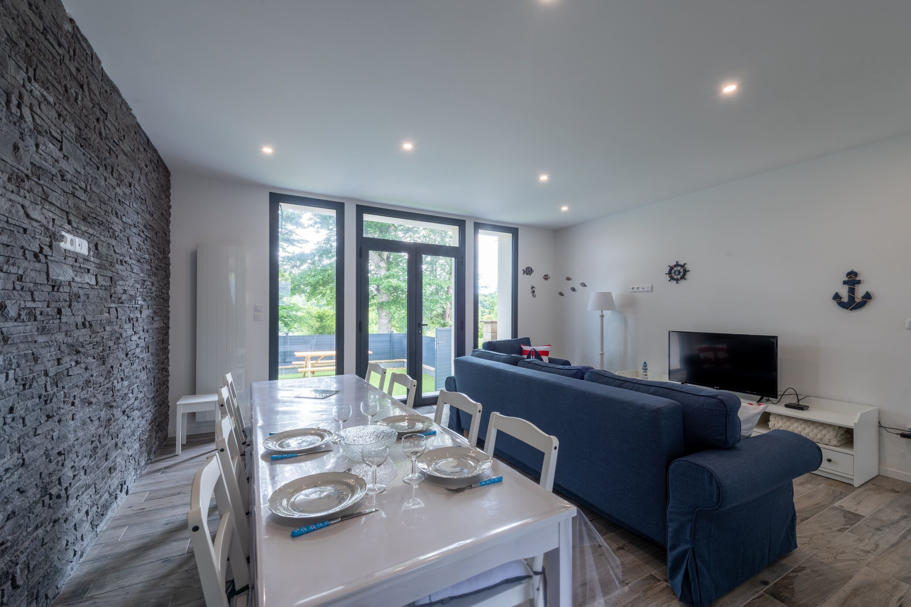 A modern living room with a dining area, a sofa, a TV, and a stone wall.
