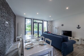 A modern living room with a dining area, a sofa, a TV, and a stone wall. - Le Beau Rivage - 1km de la Plage (Criel-sur-Mer)