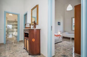 A hotel room with a wooden cabinet, a mirror, a bed, and a bathroom visible through an open door. - Villa Le Terrazze Blu (Sicilia)