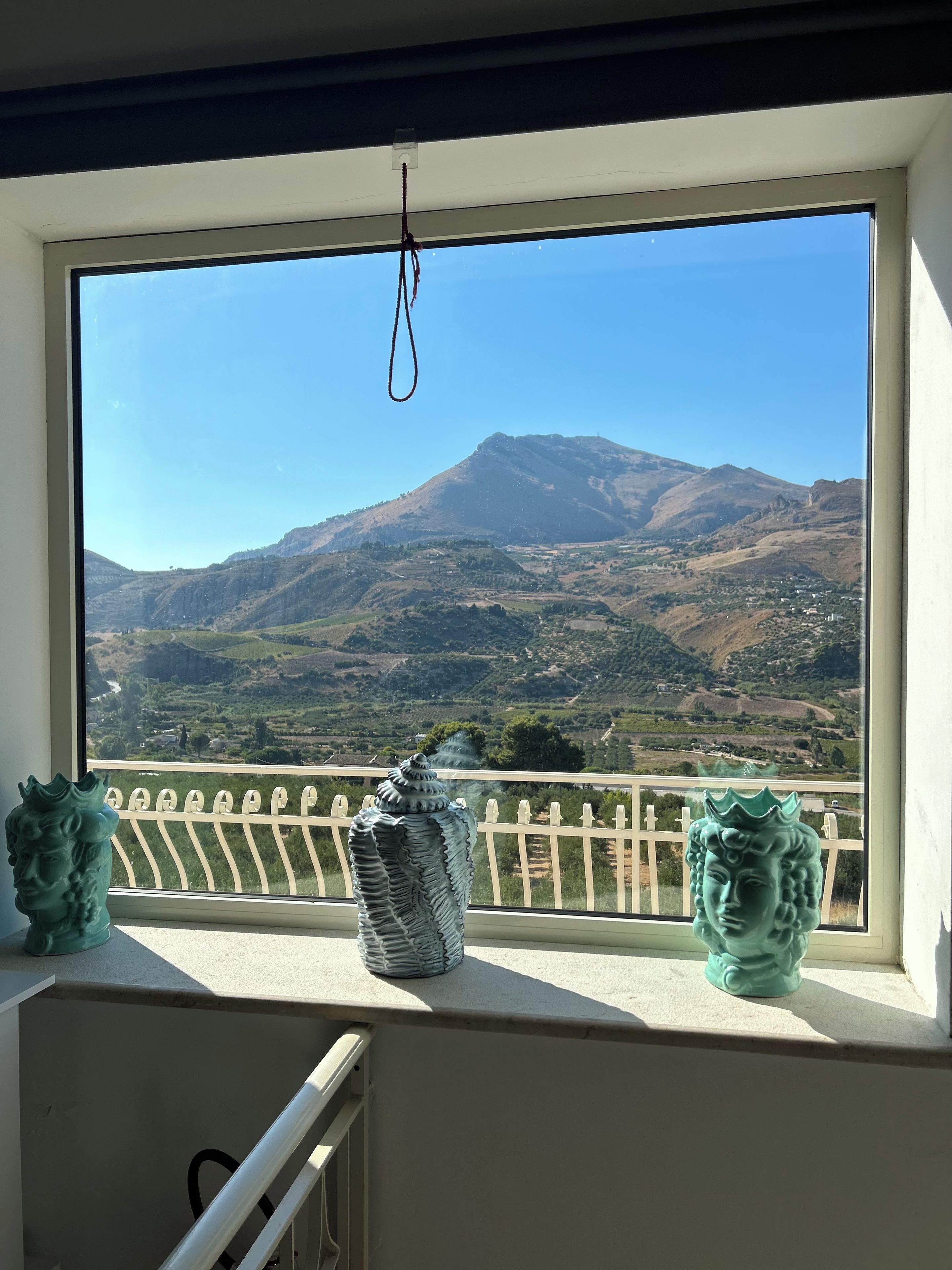 A window with a view of a mountain landscape, a white railing, and two decorative vases.