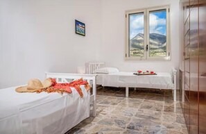A room with two beds, a window with a mountain view, a radiator, and a picture on the wall. - Villa Le Terrazze Blu (Sicilia)