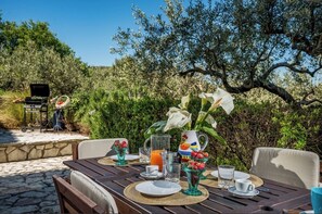 Een terras met een ontbijttafel, omgeven door groen en een heldere lucht.