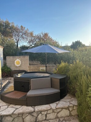 A hot tub with a semi-circular seating area, surrounded by stone flooring and greenery. - Villa Le Terrazze Blu (Sicilia)