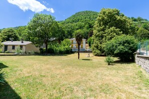 Ein Wohngebiet mit zwei Häusern, eines mit gelber Fassade und das andere mit weißer Fassade, umgeben von üppiger Vegetation und einer Hügelkette im Hintergrund.