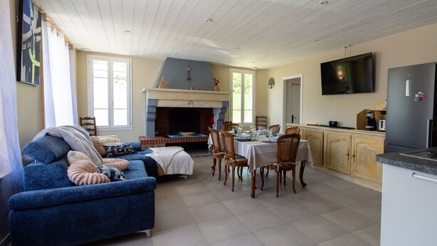Amplia sala de estar con sofá azul, comedor con mesa dispuesta para cuatro, cocina con refrigerador y televisión, además de una chimenea.