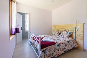 Un dormitori amb un llit, un panell de capçal de fusta, una finestra amb cortines i una porta que dóna a un bany.