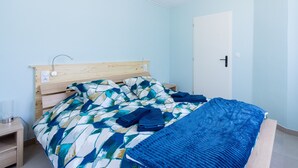 Un dormitorio con cabecera de madera, cama con colcha estampada, manta azul y mesita de noche con lámpara.