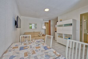 Zona de menjador amb taula per a quatre, un sofà, un armari blanc i un mirall a la paret.