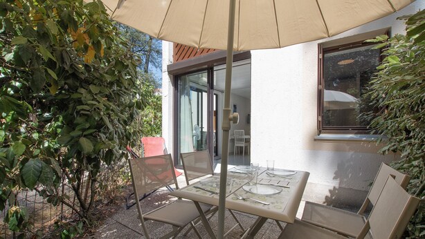 Eine Terrasse im Freien mit Tisch und Stühlen, eine Glastür und Blick ins umliegende Grün.