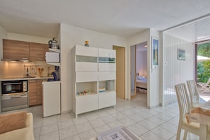 Een knus woongedeelte met een kitchenette, een witte inbouwkast en een eethoek met stoelen.