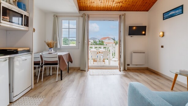 Een ruimtelijk ingerichte leefruimte met kitchenette, eethoek en een aan de muur bevestigde televisie.