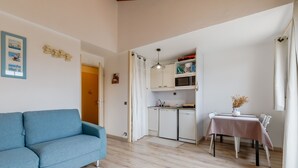 Een knus woongedeelte met een bank, kitchenette, eettafel en een klein decoratief vaasje.