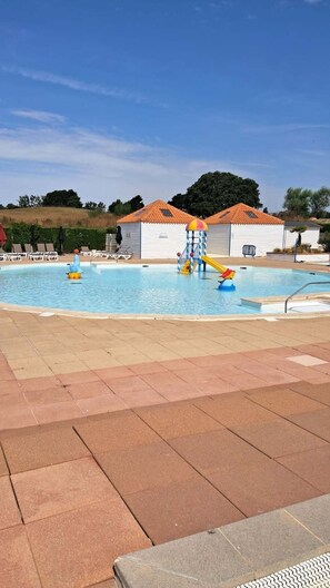 Une piscine avec un toboggan et des jeux gonflables, entourée de chaises longues et d’un espace abrité.