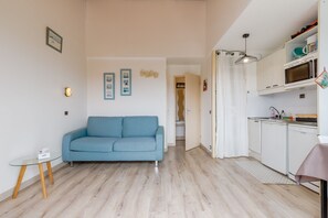 Un espace de vie compact comprenant un canapé, une kitchenette et une porte donnant accès à une salle de bain.