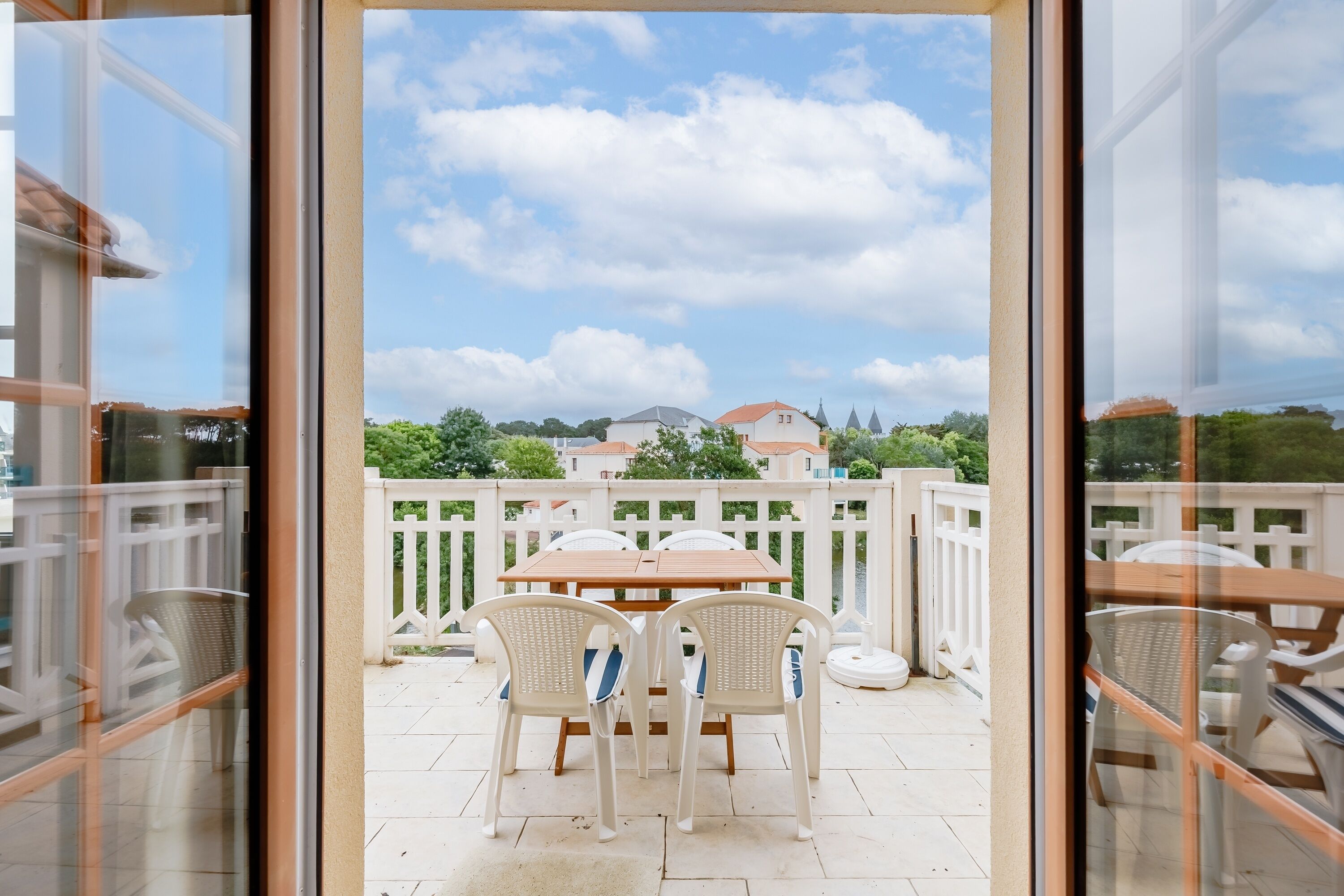 Un patio al aire libre con una mesa y sillas, una cerca blanca y vistas de un edificio con techo rojo.