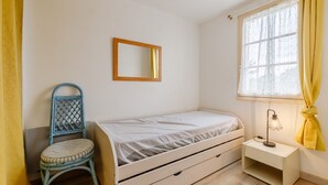Een slaapkamer met een enkel bed, een stoel, een nachtkastje, gordijnen voor het raam en een spiegel aan de muur.