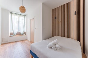 Ein Schlafzimmer mit Bett, einem Fenster mit Vorhängen, einer Wand aus Holzlamellen und einer Pendelleuchte.