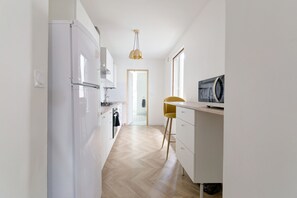 A modern kitchen with white cabinetry, a wooden floor, and a yellow chair. - Le Cocon Champenois - Joli appt proche du centre (Reims)