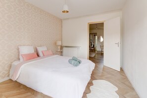 A bedroom with a large bed, a radiator, a white door, and a hallway leading to another room. - Le Cocon Champenois - Joli appt proche du centre (Reims)