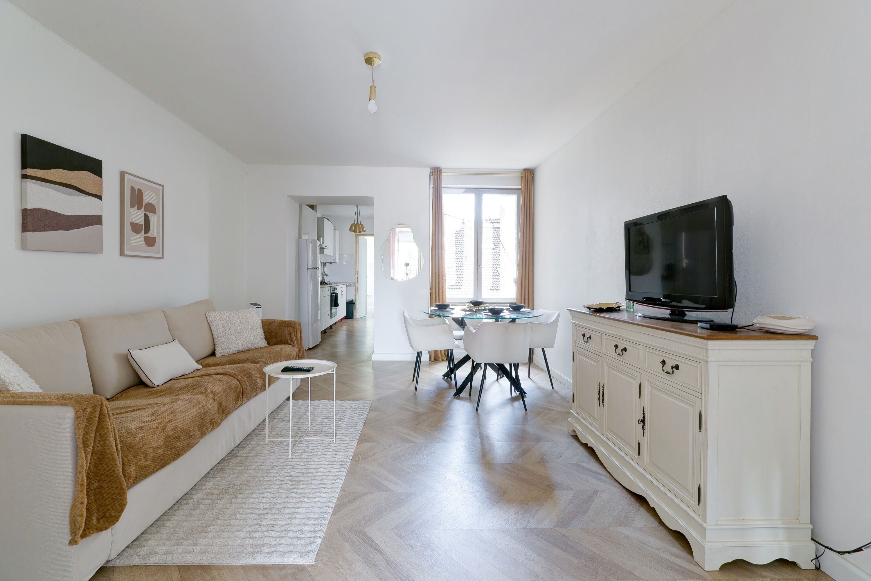 A modern living room with a sofa, TV, dining table, and white cabinetry.