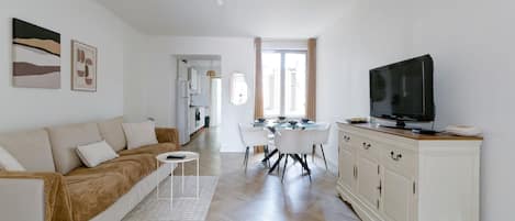 Ein modernes Wohnzimmer mit Sofa, Fernseher, Esstisch und weißen Schränken.