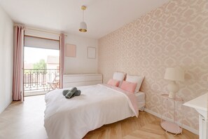 Ein Schlafzimmer mit einem Bett, einem Nachttisch, einer Lampe, einem Fenster mit Vorhängen und einer Wand mit Muster.