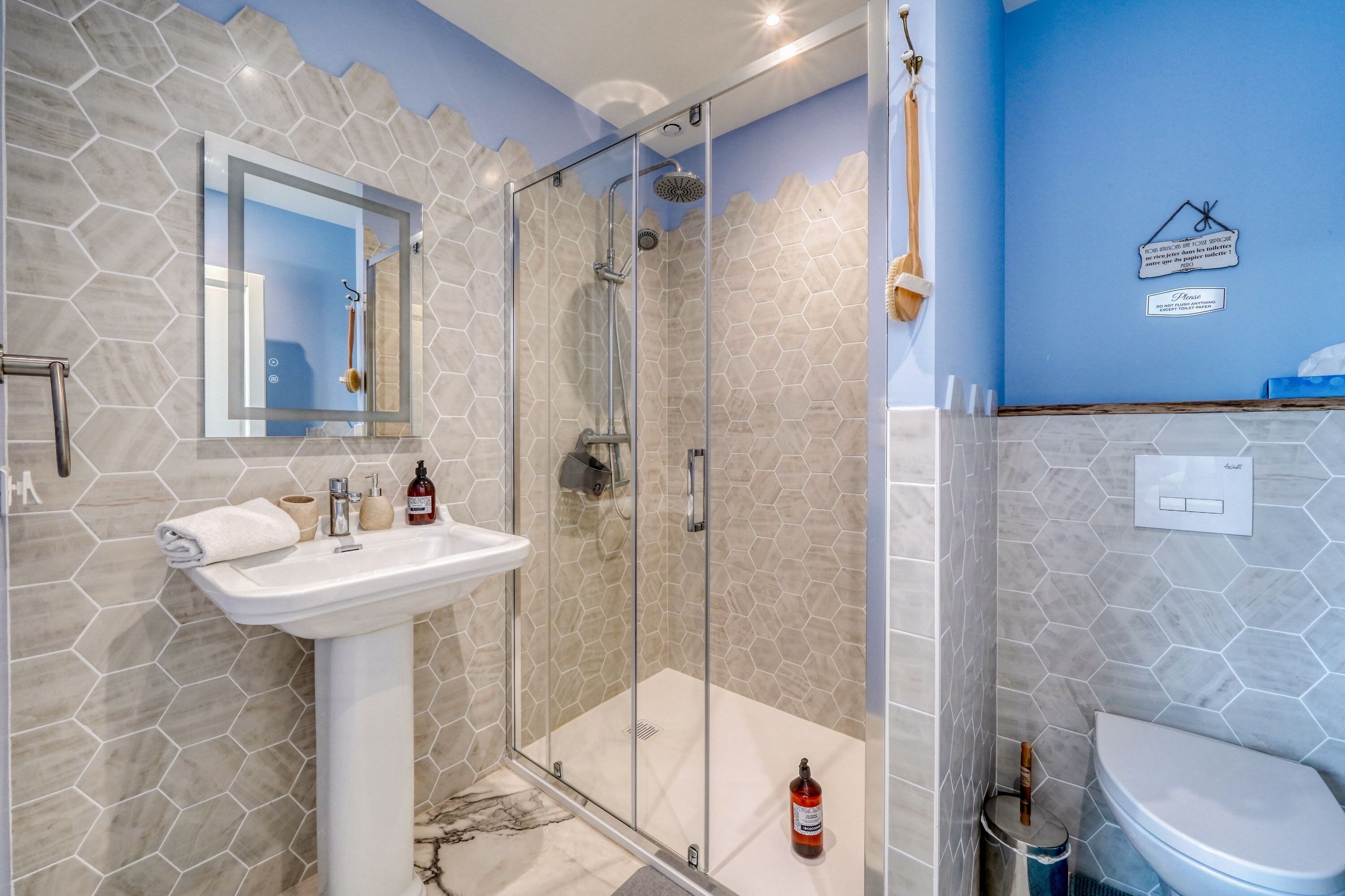 Een badkamer met een douchecabine van glas, een witte wastafel en een blauwe accentmuur.