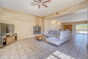 Ein großzügiges Wohnzimmer mit einem großen Flachbildfernseher, einem Kamin, einer Couch und einem Deckenventilator.