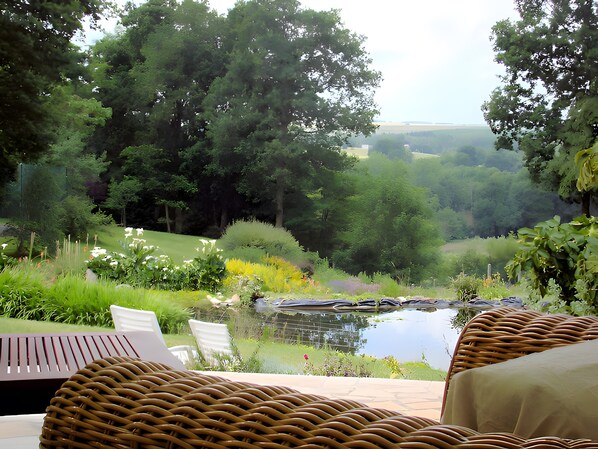 A garden with a pond, wicker furniture, and a view of the countryside.